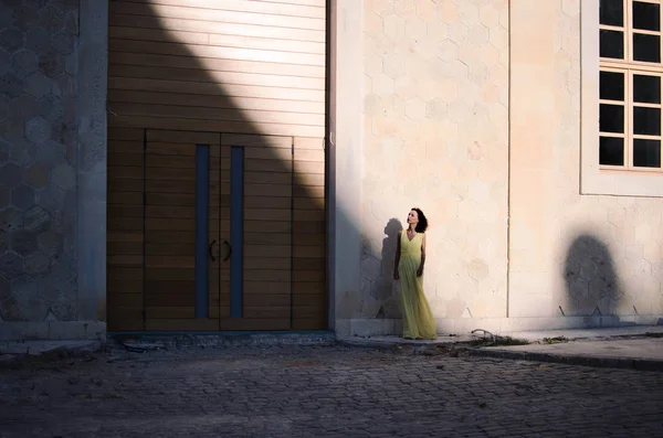 Woman in shadow lights in front of big architecture with wooden doors.