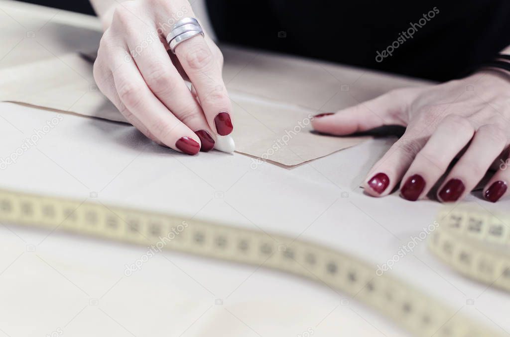 close-up of female hands with chalk. Tailor working on clothes pattern on the table
