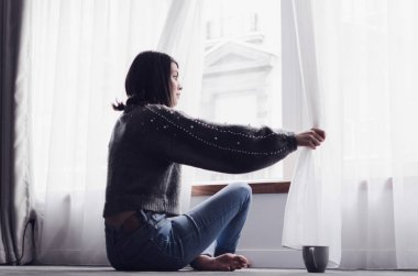 Genç kadın veya açık pencerenin onun oturma odası, instagram tonlama, yeni gün kavramı içinde dinlendirici halı üzerinde evde oturan kız