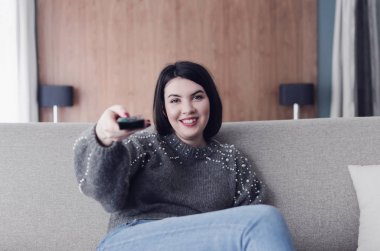Evde TV izlerken, bir uzaktan kumanda tutan kadın. Gülümseyen kadın kanepede