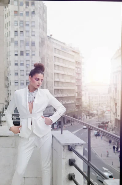 young woman in designer white suit posing on balcony