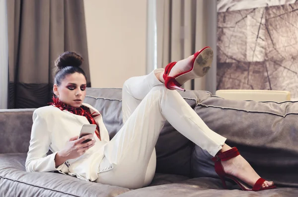 young woman in white suit and red necklace using smartphone