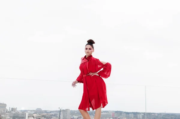 ポーズの屋根の上の赤いドレスの若いブルネットの女性 — ストック写真