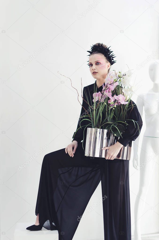 Young woman in black wide pants posing over white background with maniquine 
