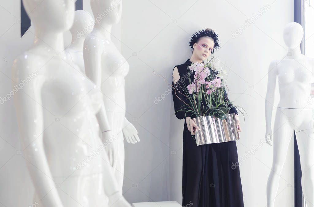 Young woman in black wide pants posing over white background with maniquines