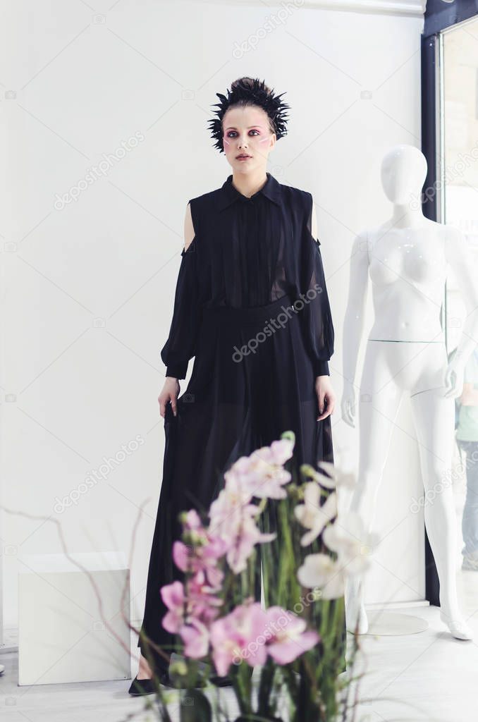 Young woman in black wide pants posing over white background with maniquine 