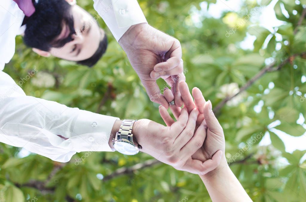 Picture of man putting engagement silver ring on womans hand, outdoors