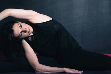 Fitness 'e adanmıştır. Siyah spor giysili güzel bir kadının yerde otururken esneme hareketleri.