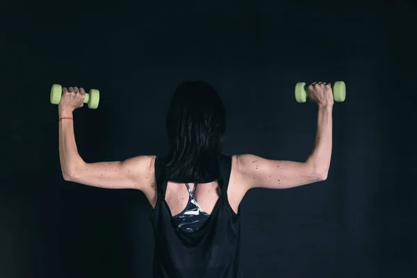 Athletic woman doing exercise for arms. Working out with dumbbells on black background