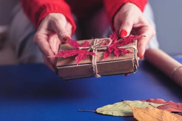 葉で装飾された手作りの段ボール箱を示す女性の手の作物ビュー — ストック写真