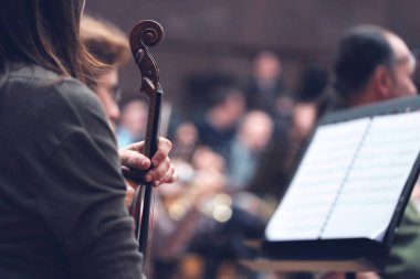 Orkestranın kesilmiş resmi, bir grup insan, bulanık notalara bakan bir kızın yakın çekimi. Müzik aleti tutuluyor