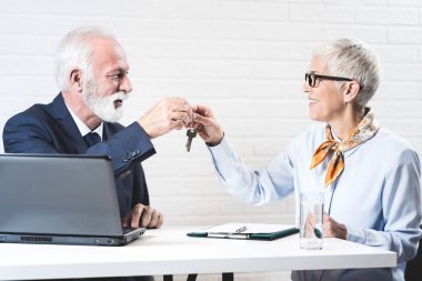 Senior lady taking keys from older male real estate agent during meeting after signing rental lease contract  clipart