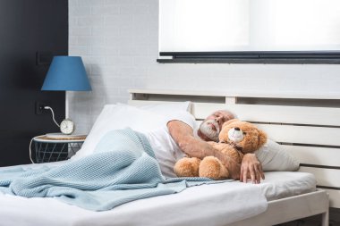 Beyaz saçlı ve sakallı yaşlı adam yatak odasında oyuncak ayıyla uyuyor. Emekli ve yalnız bir adamın gecelerini düşün.