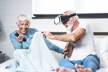 Yatak odasında VR gözlüklü yaşlı sakallı adam karısıyla eğleniyor.