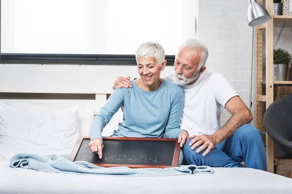 Senior Happy Couple Sitting Bed Pajamas Woman Writing Message Panel — ストック写真