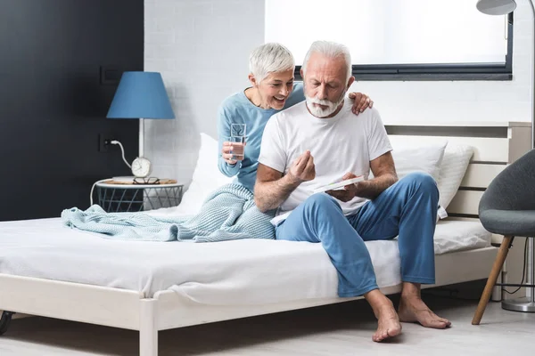 上了年纪的夫妇在家里 年长的灰发男人和女人在床上坐着吃药 概念夫妻服用维生素 — 图库照片