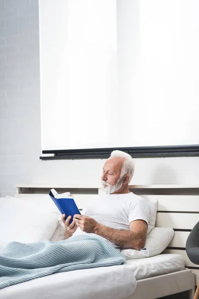 Ανώτερος Άντρας Στο Σπίτι Διαβάζει Βιβλία Στο Κρεβάτι Πριν Κοιμηθεί — Φωτογραφία Αρχείου