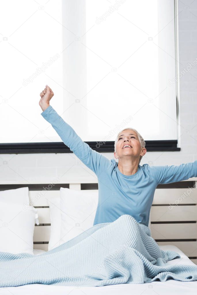 Happy grey hair senior woman stretching in bed after wake up in morning in bed