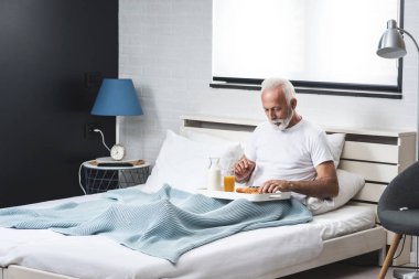 Uyandıktan sonra yatakta kahvaltı eden mutlu kıdemli adam.