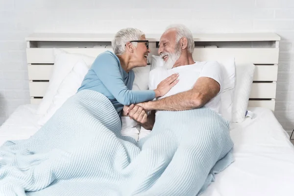 Romantic senior couple laughing while lying in bed at home