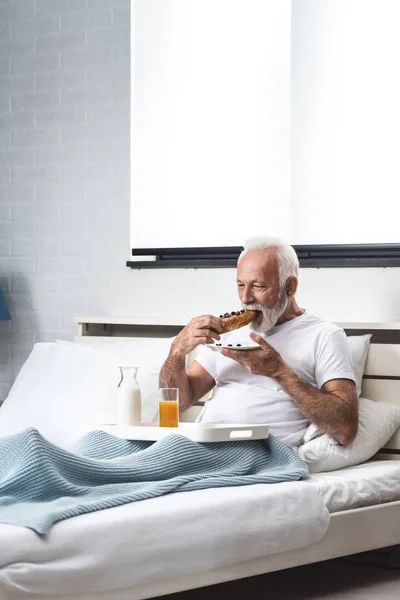 Šťastný Senior Muž Snídaní Posteli Probuzení Jíst Čokoládový Croissant Mlékem — Stock fotografie