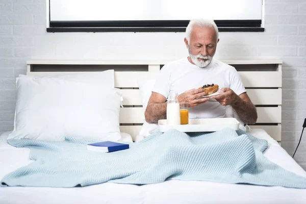 Boldog Nyugdíjas Férfi Reggelizik Ágyban Miután Felébredt Csokis Croissant Eszik — Stock Fotó