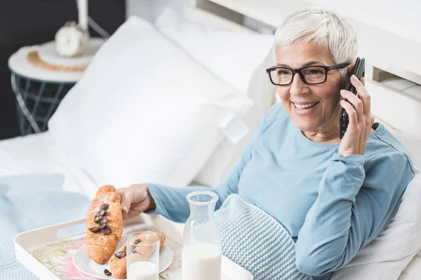 Mujer Mayor Desayunando Cama Una Mano Croissant Chocolate Otro Teléfono — Foto de Stock