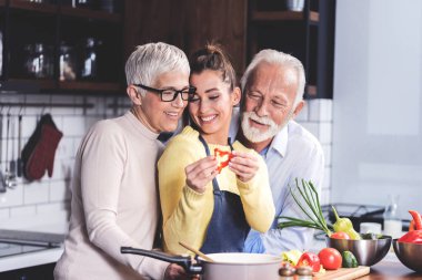 Mutlu aile mutfakta öğle yemeği için sebze salatası hazırlar. Genç kız tatlı biberle eğleniyor. Sağlıklı beslenme ve diyet gıda kavramı