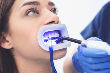 Klinikteki dişçide çalışan bir kadının yakın plan portresi. Ultraviyole ışık feneriyle diş beyazlatma prosedürü.