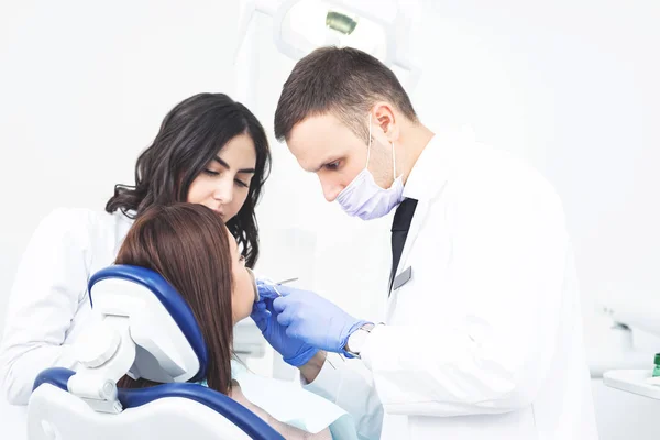 歯科医のオフィスでは 医師とアシスタントが若い女性患者に歯科修復を行っています 白い背景にスペースをコピー — ストック写真