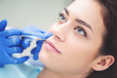 Kadın dudaklarında enjeksiyon yapma güzellik uzmanı el kapatın. Şırınga elinde var. Genç güzel kadın yordamı ile zevk alıyor