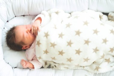 Yeni doğmuş bebek, beyaz battaniyeyle kaplı bir emzik ile yuvasında uyuyakaldı..