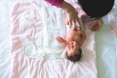 Kendini bebek bezine sararken ağlayan yeni doğan bebeğinin yakın plan fotoğrafı. Anne elleriyle bebeği giydirirken çekilmiş bir resim. Kopyalama alanı ile resim