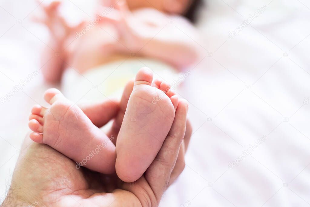 Cropped picture of daddy's hand holding the feet of his newborn baby daughter. Copy space picture. Blurred baby, closeup baby's soles