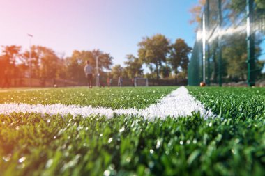 Güneşli bir günde, gradyan ile futbol sahası. Çocuklar futbol oynuyor. Bokeh 'in dibi. Beyaz çizgili yeni yapay çim.