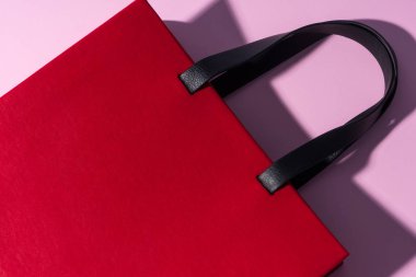 Pembe arka planda siyah saplı kırmızı deri çanta. Logo ya da reklam için boş yer. Alışveriş için paket.