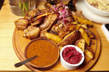 Ahşap bir tabakta fırında patates ve ızgara pirzola. İki çeşit sosla servis edilir. İştah açıcı taze yemek. Yetersiz beslenme konsepti fotoğrafı.