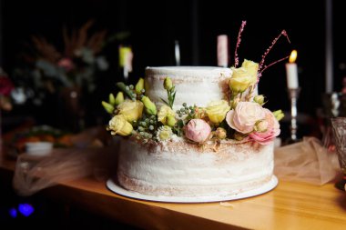 Çiçeklerle süslenmiş güzel bir düğün pastası. Ahşap masada pembe ve sarı güllü el yapımı tatlı..