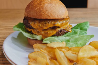 Duble peynirli ve salatalı sığır etli burger. Beyaz tabakta patates kızartmalarıyla servis ediliyor. Amerikan mutfağı..