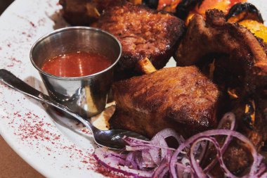 Ahşap bir şişte ızgara sebzeli ve kırmızı baharatlı soslu leziz barbekü eti. Beyaz tabakta soğanla servis ediliyor. Yakın çekim..