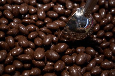 Almonds in chocolate glaze. Nuts in milk chocolate. Brown jelly beans dragee background. Candy shop. Metal scoop inside sweets. Horizontal photo.