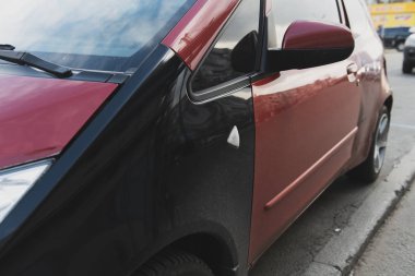 Siyah kanatlı bir kaza sonrası küçük kırmızı bir araba. Yan etki. Yanlış renk araba parçaları. Yakın çekim..