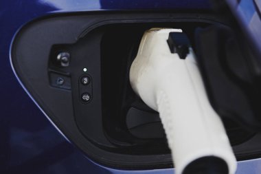Mavi elektrikli arabadaki beyaz eklenti bağlantısı. Şarj olurken araba. Ekolojik ulaşım. Şarj göstergesi. Yakın çekim..