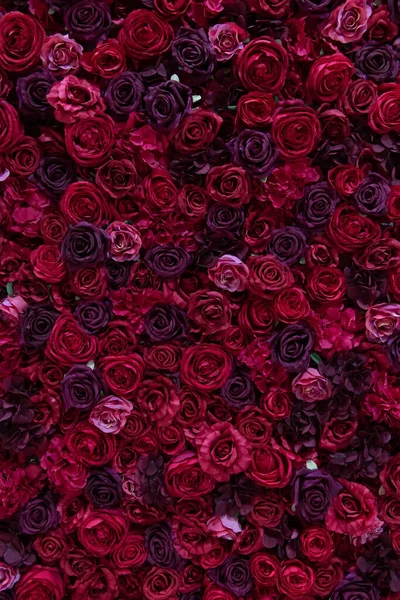 Red and purple paper roses background. Wall made of paper flowers. Floral interior. Vertical photo.