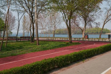 Nehir kenarındaki koşu pisti olan güzel boş bir park. Dinlenmek ve koşmak için mükemmel bir yer. Güneşli bir gün. Karantina sırasında park et.