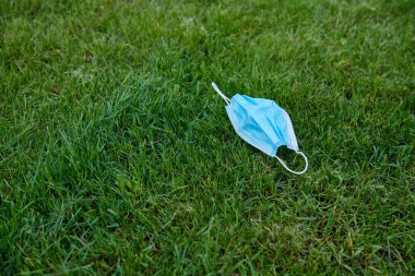 Mavi yüz maskesi yeşil çimlerin üzerinde yatıyor. Çevre kirliliği konsepti fotoğrafı. Salgın koronavirüs sorunları. Hastalığın sonu. Metin için boş alan.