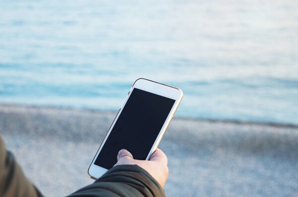мужская рука держит смартфон на фоне океана, р
