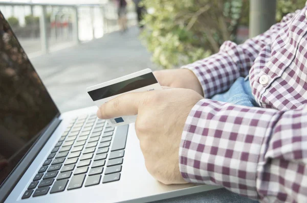 man holding credit card and laptop staying outside and paying on
