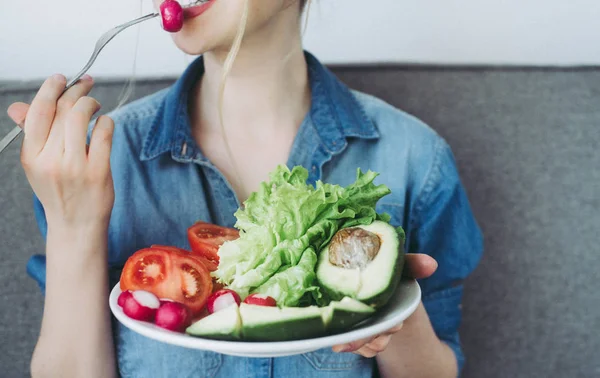 Jeune femme souriante mangeant des légumes frais à la maison. Manger végétalien — Photo