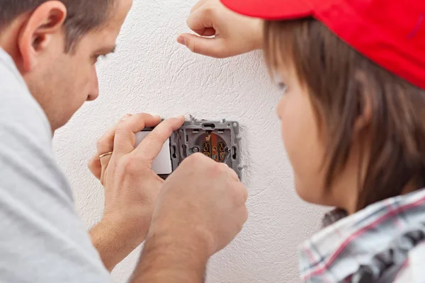 Young boy watches as his father installs an electrical wall sock